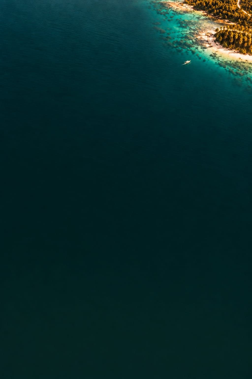 Aerial view of a bangka boat approaching a palm-covered islet off Siargao's coast at golden hour