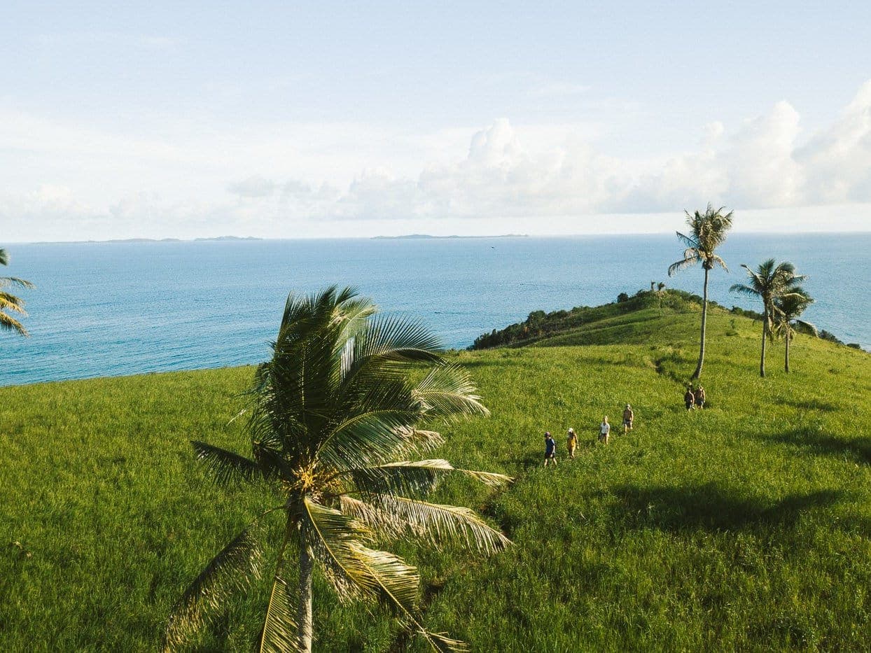 Hikers crossing a grassy, palm-dotted hilltop on Corregidor Island above the open sea